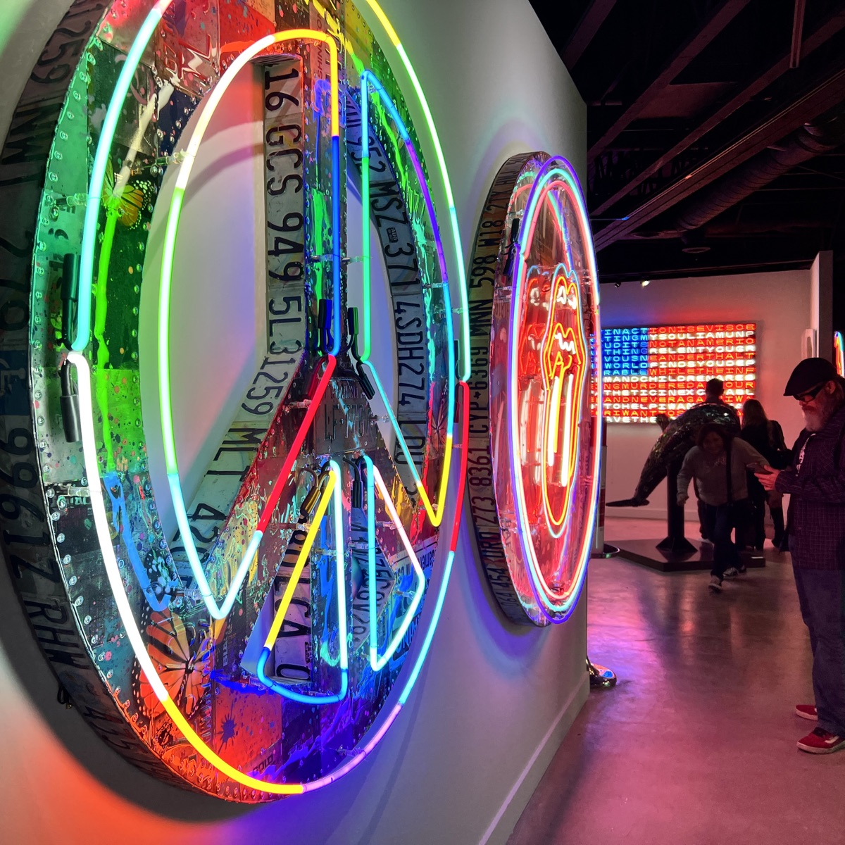 Neon peace-sign artwork by Risk in a contemporary gallery