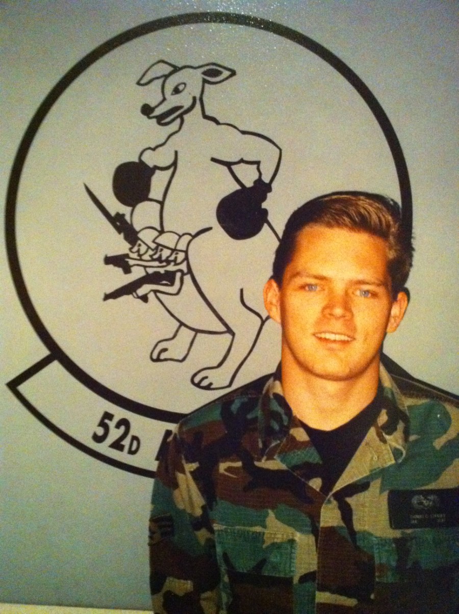 Tommy Strader in U.S. Air Force camouflage fatigues in front of the 52d squadron emblem